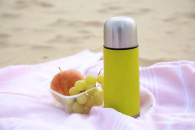Photo of Metallic thermos with hot drink, fruits and plaid on sandy beach