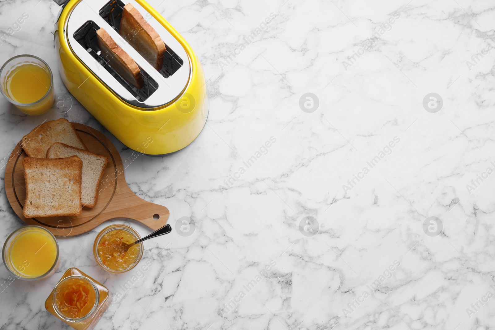 Photo of Toaster with roasted bread, glasses of juice and jam on white marble table, flat lay. Space for text