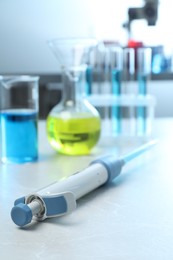 Laboratory analysis. Micropipette and different glassware with liquids on light grey marble table