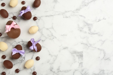 Photo of Sweet chocolate eggs and candies on white marble table, flat lay. Space for text