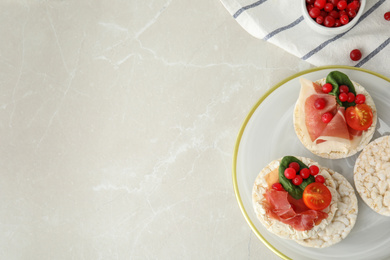 Photo of Puffed rice cakes with prosciutto, berries and basil on grey marble table, flat lay. Space for text