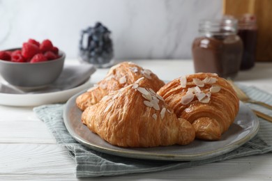 Photo of Delicious croissants with almond flakes on white wooden table, closeup