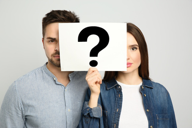 Photo of Couple holding question mark sign on light background