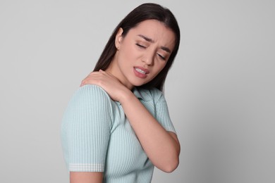 Photo of Young woman suffering from pain in shoulder on light grey background. Arthritis symptoms
