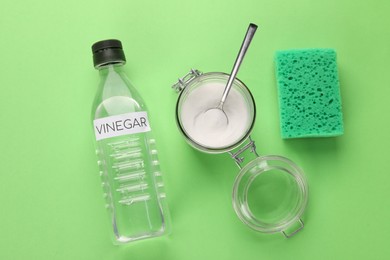 Photo of Eco friendly natural cleaners. Vinegar in bottle, sponge and jar of soda on green background, flat lay