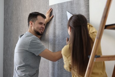 Photo of Couple hanging stylish gray wallpaper in room