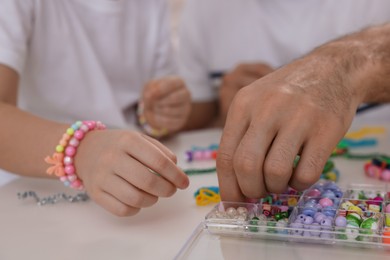 Photo of Father with his daughter making beaded jewelry at table, closeup