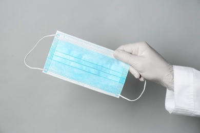 Photo of Doctor in medical gloves holding protective mask on light grey background, closeup