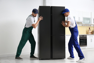 Photo of Professional workers carrying modern refrigerator in kitchen