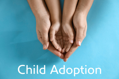 Image of Mother holding hands with her child on blue background, top view. Adoption concept