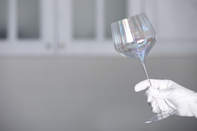 Photo of Person in white glove checking cleanliness of glass indoors, closeup. Space for text