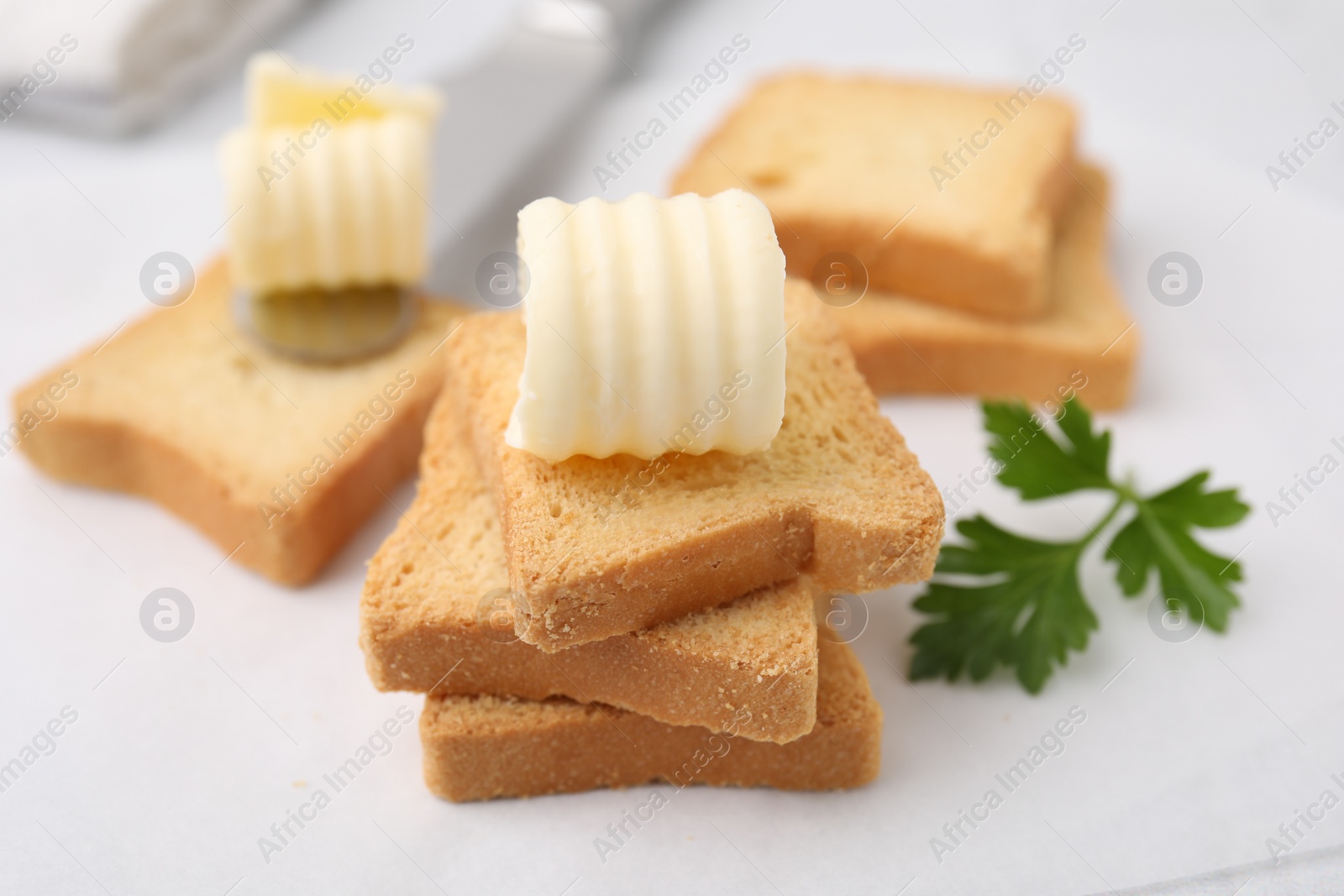 Photo of Tasty butter curls, knife and pieces of dry bread on white table, closeup