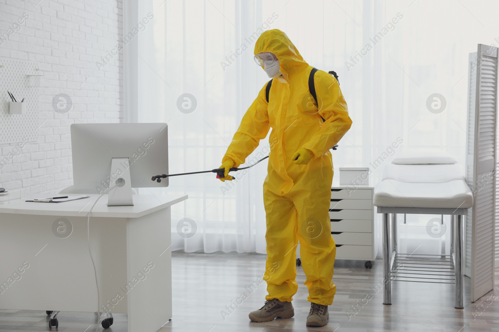 Photo of Employee in protective suit sanitizing doctor's office. Medical disinfection