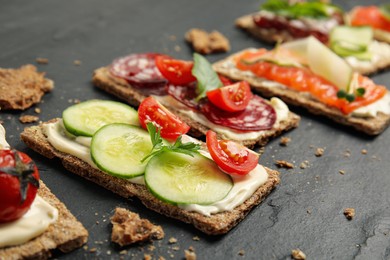 Photo of Fresh rye crispbreads with different toppings on black table, closeup