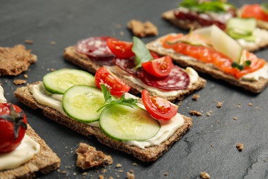 Fresh rye crispbreads with different toppings on black table, closeup