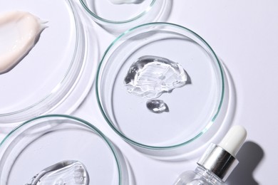 Photo of Petri dishes with samples of cosmetic serums and bottle on white background, flat lay