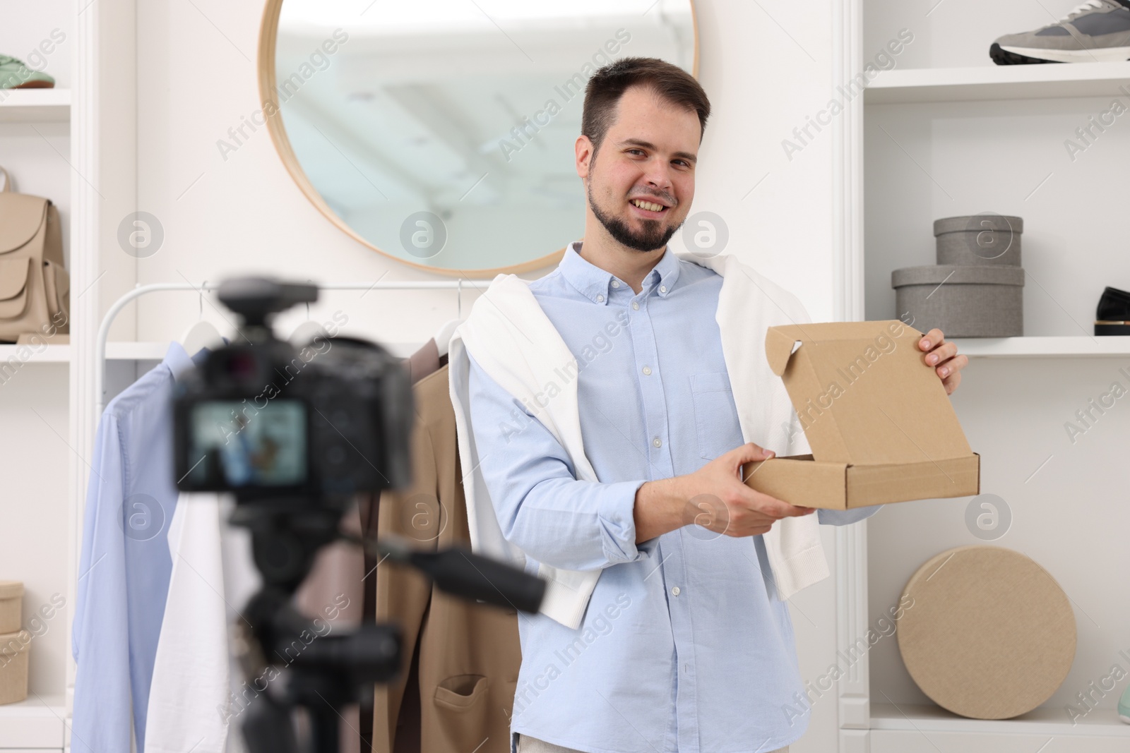 Photo of Smiling fashion blogger opening cardboard box while recording video at home