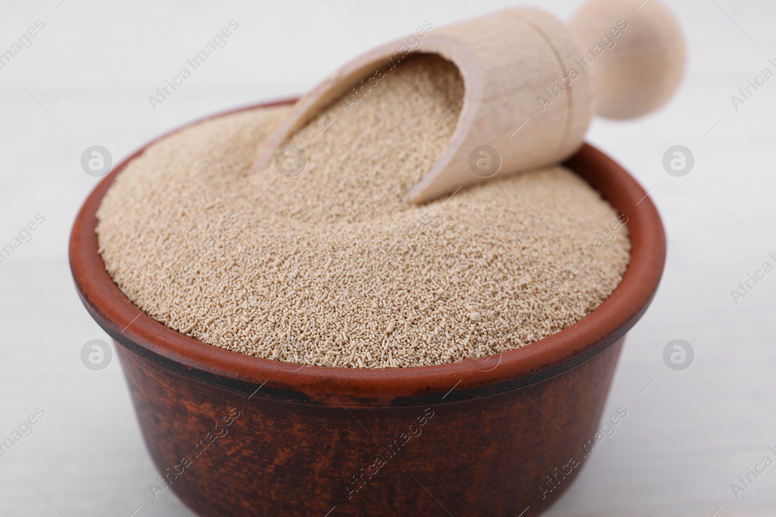 Photo of Bowl and scoop with active dry yeast on white wooden table, closeup