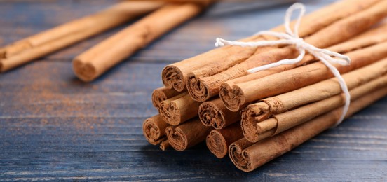 Image of Aromatic cinnamon sticks on blue wooden table, closeup. Banner design