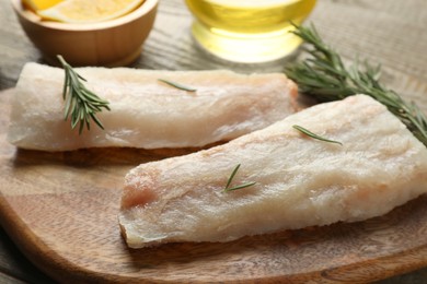 Photo of Fresh raw cod fillets with rosemary on wooden table, closeup