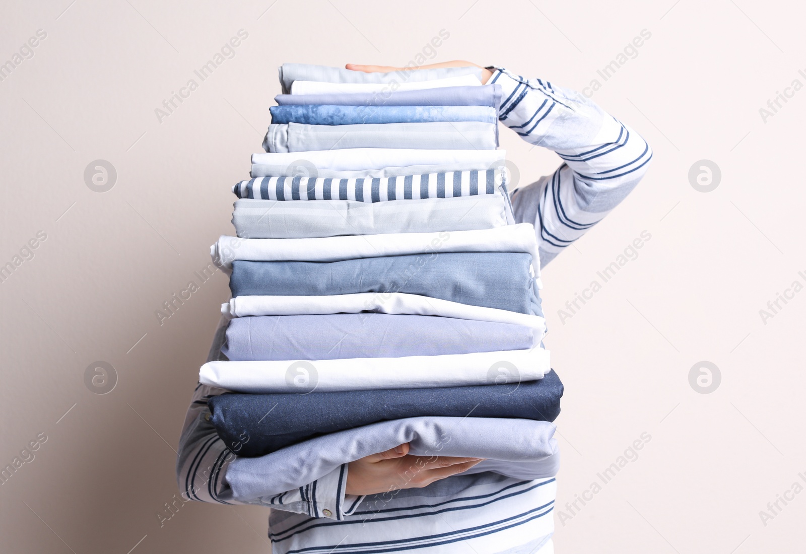 Photo of Woman holding stack of clean bed linens on beige background