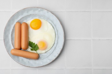 Photo of Delicious boiled sausages, fried eggs and parsley on white tiled table, top view. Space for text