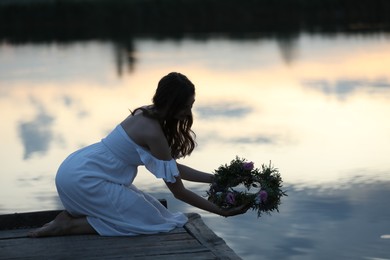Photo of Young woman putting wreath made of beautiful flowers in water