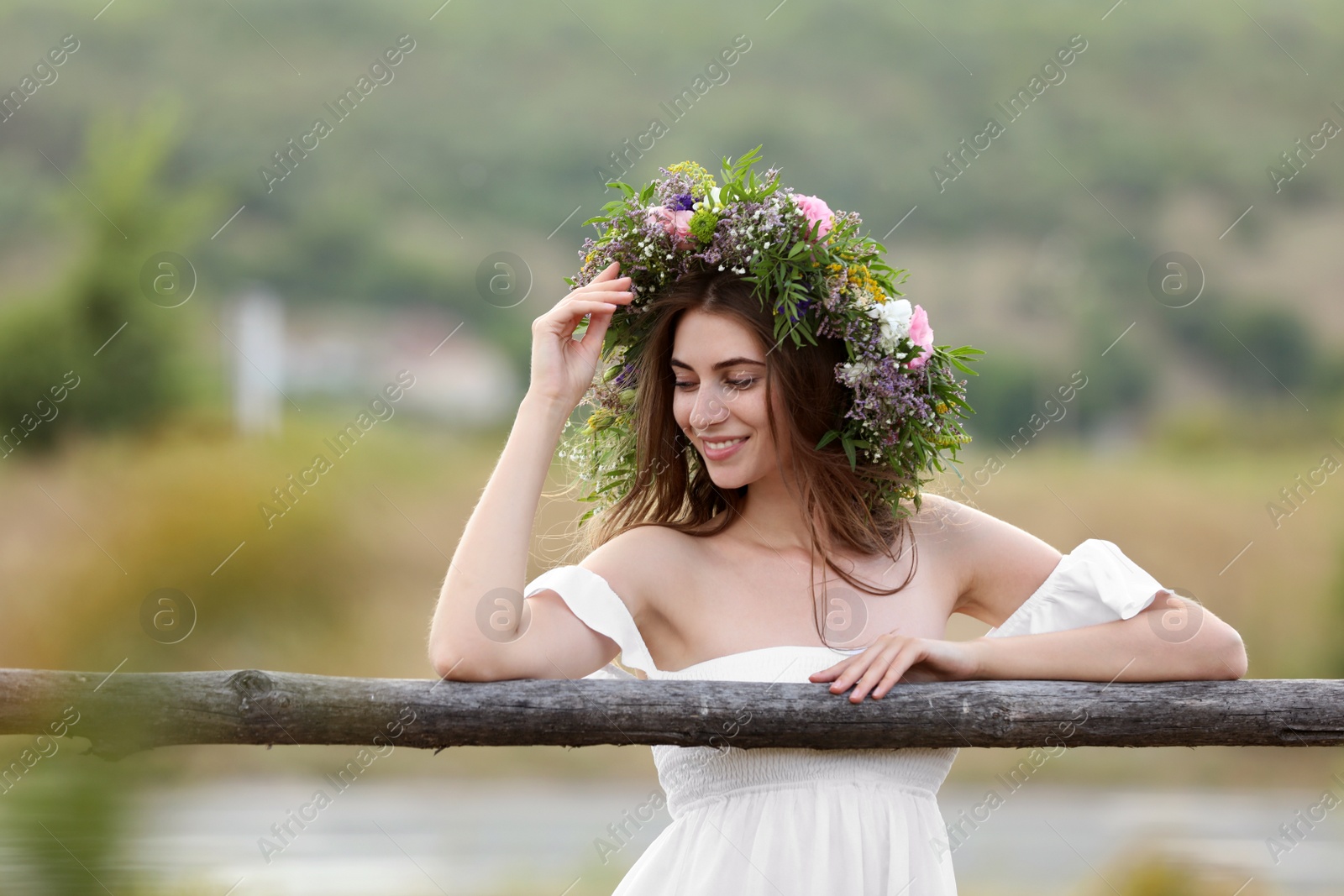 Photo of Young woman wearing wreath made of beautiful flowers near wooden fence