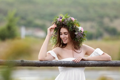 Young woman wearing wreath made of beautiful flowers near wooden fence