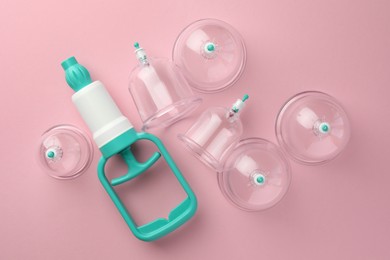 Photo of Plastic cups and hand pump on pink background, flat lay. Cupping therapy