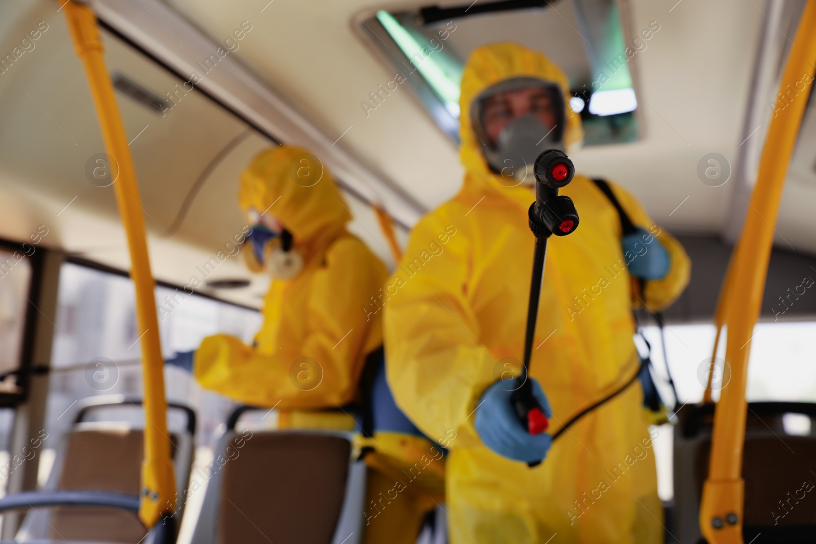 Photo of Public transport sanitation. Workers in protective suits disinfecting bus salon, focus on spray machine nozzle