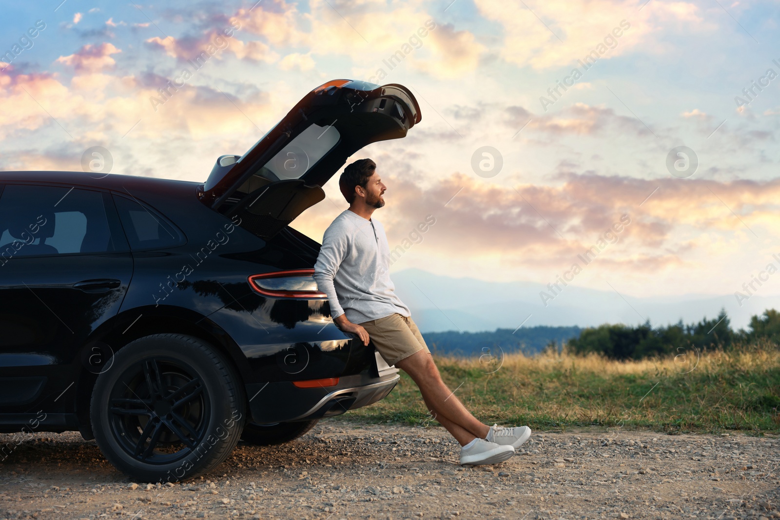 Photo of Happy man sitting in trunk of modern car on roadside outdoors