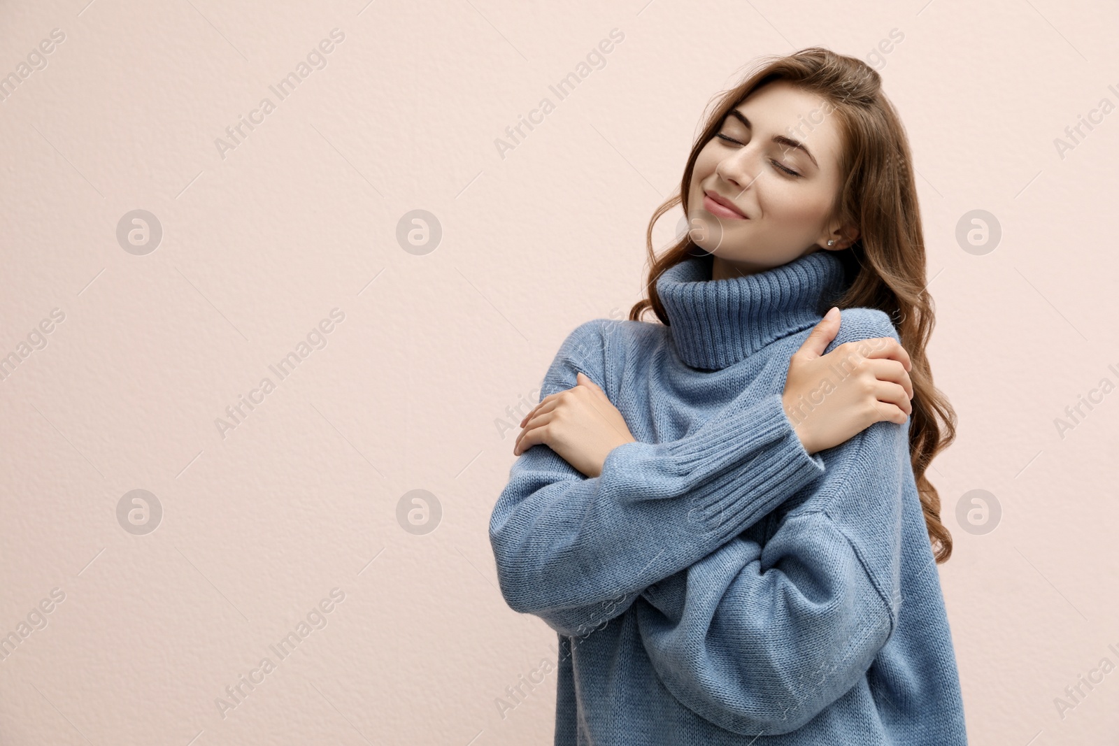 Photo of Beautiful young woman wearing warm blue sweater on light pink background. Space for text