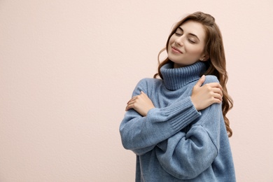 Beautiful young woman wearing warm blue sweater on light pink background. Space for text