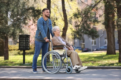 Senior woman in wheelchair with young man at park