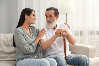 Senior man with walking cane and young woman on sofa at home