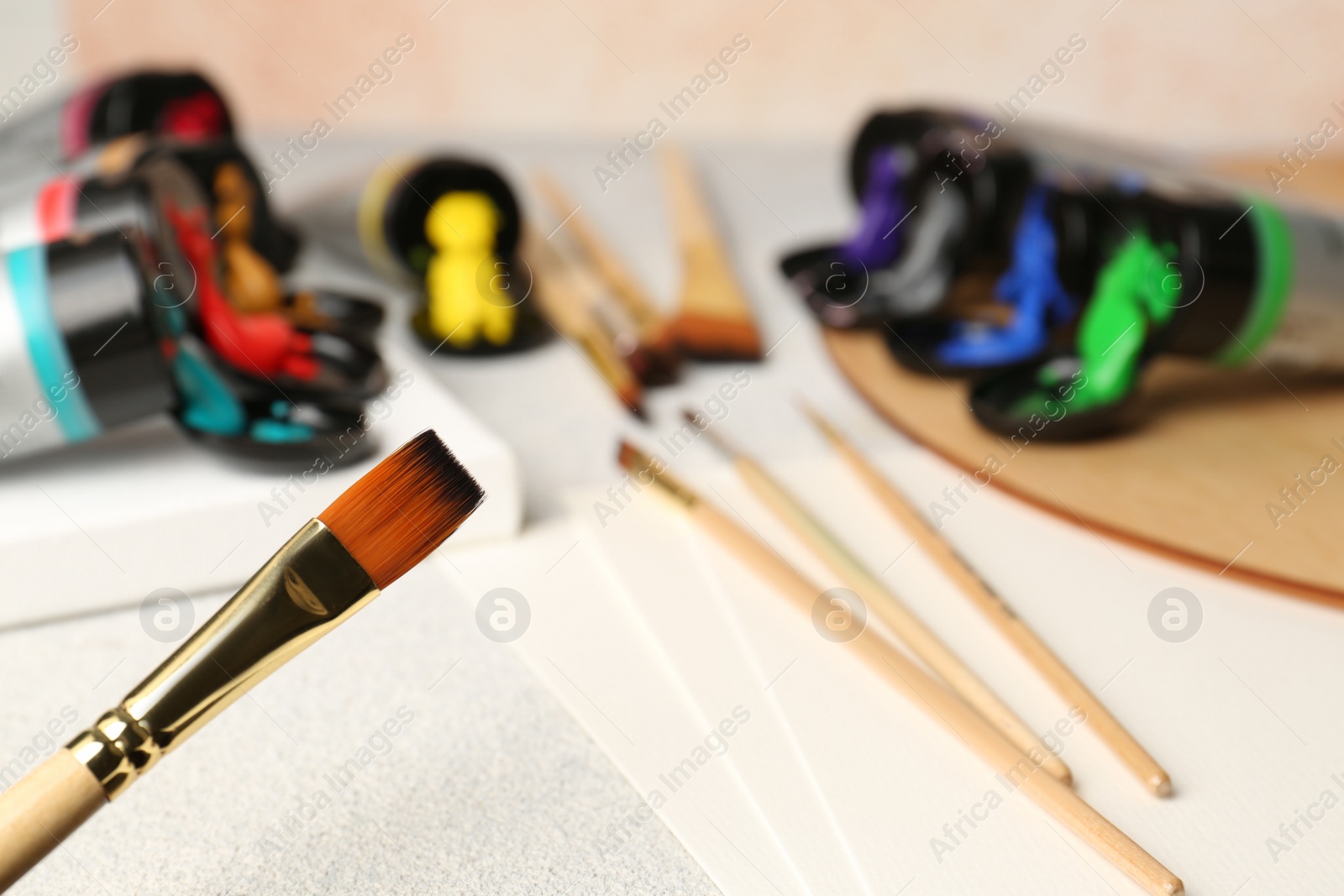 Photo of Tubes of colorful paints and brushes on textured table, closeup