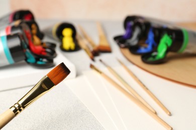 Tubes of colorful paints and brushes on textured table, closeup