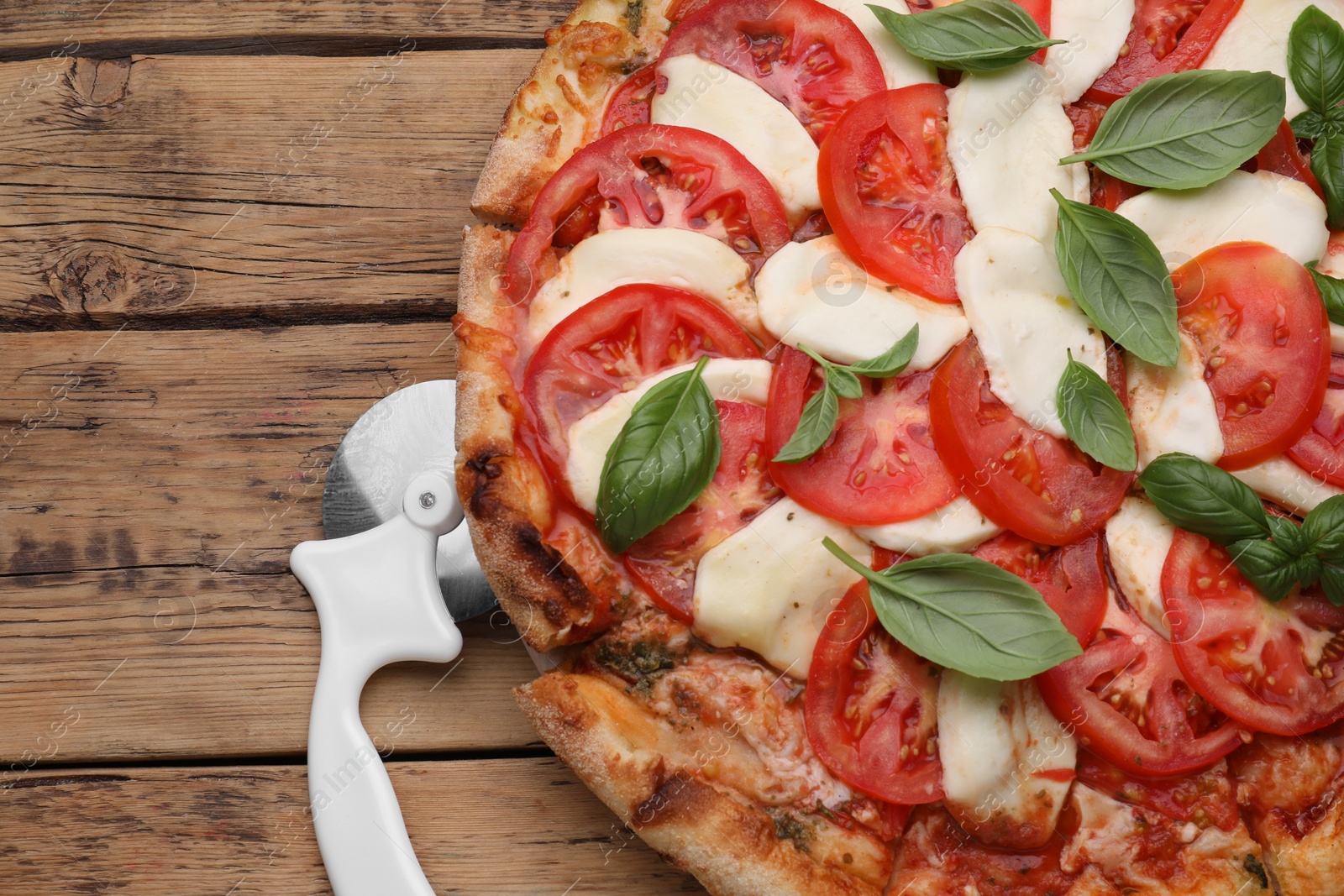 Photo of Delicious Caprese pizza and cutter on wooden table, flat lay