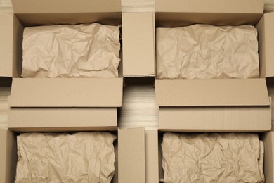 Photo of Many open cardboard boxes with crumpled paper on wooden floor, flat lay