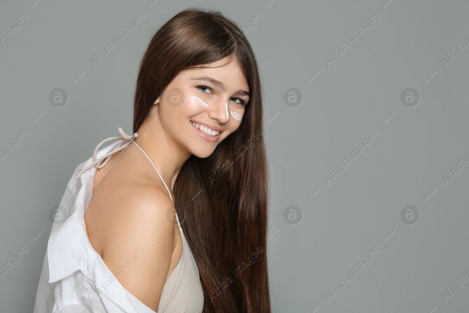 Photo of Teenage girl with sun protection cream on her face against grey background. Space for text