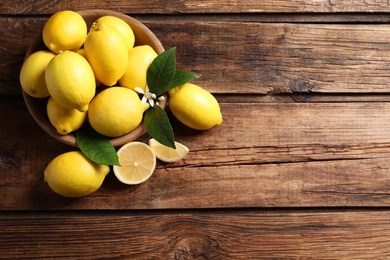 Photo of Many fresh ripe lemons with green leaves on wooden table, flat lay. Space for text