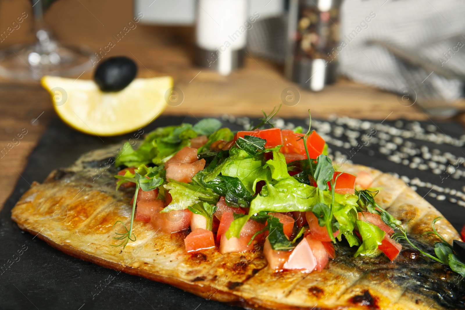 Photo of Delicious grilled fish with vegetables on slate plate, closeup