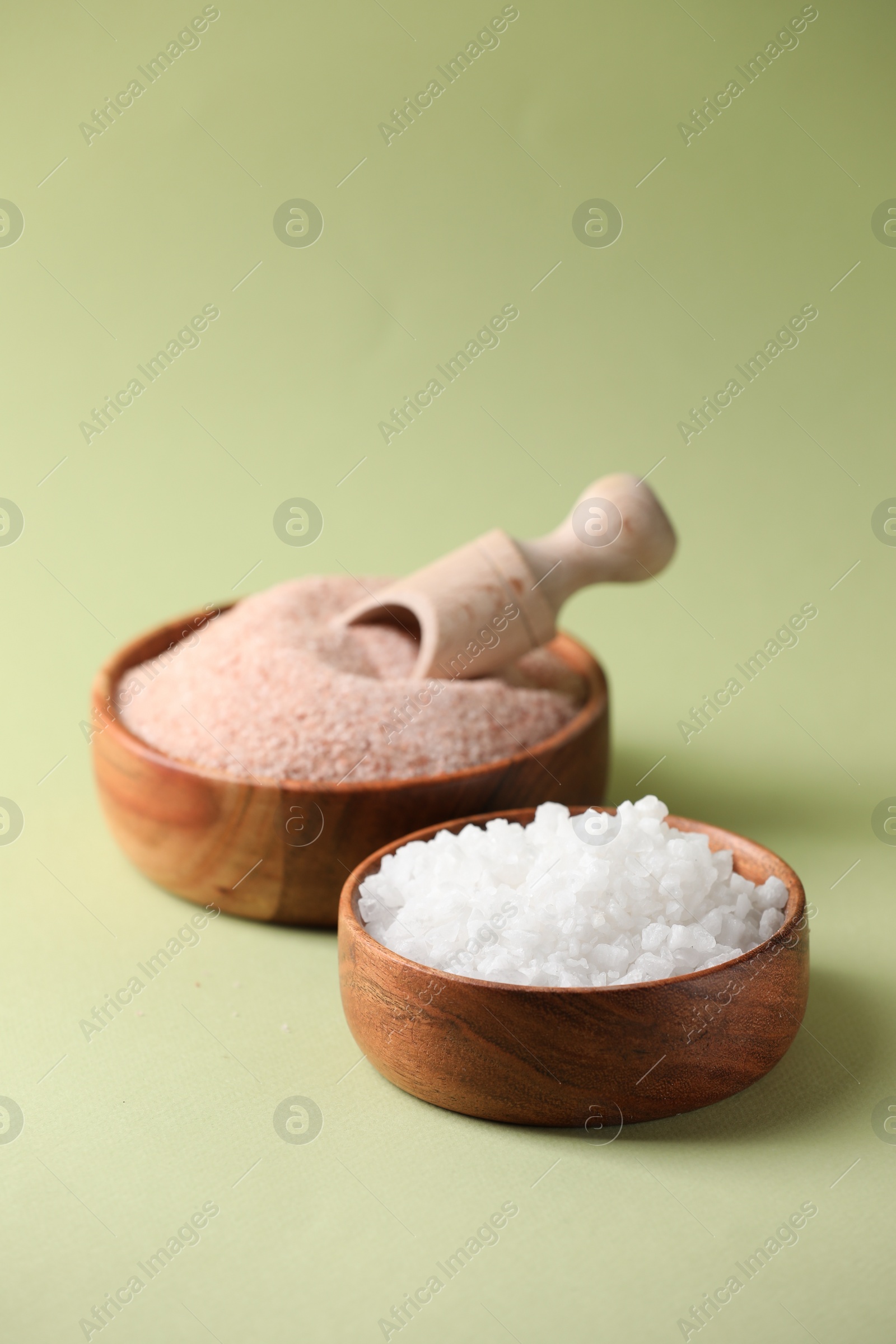 Photo of Different salt in bowls and scoop on green background