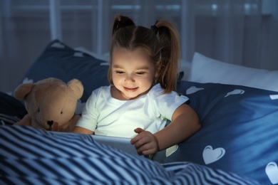 Photo of Beautiful little girl with gadget and toy in bed at night. Bedtime schedule