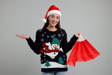Photo of Young woman in Christmas sweater and Santa hat with shopping bags on grey background