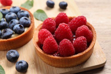 Photo of Tartlet with fresh raspberries on wooden board, closeup. Delicious dessert