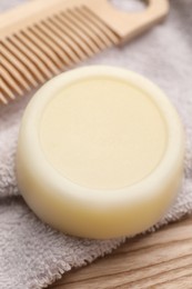 Photo of Solid shampoo bar and towel on wooden table, closeup