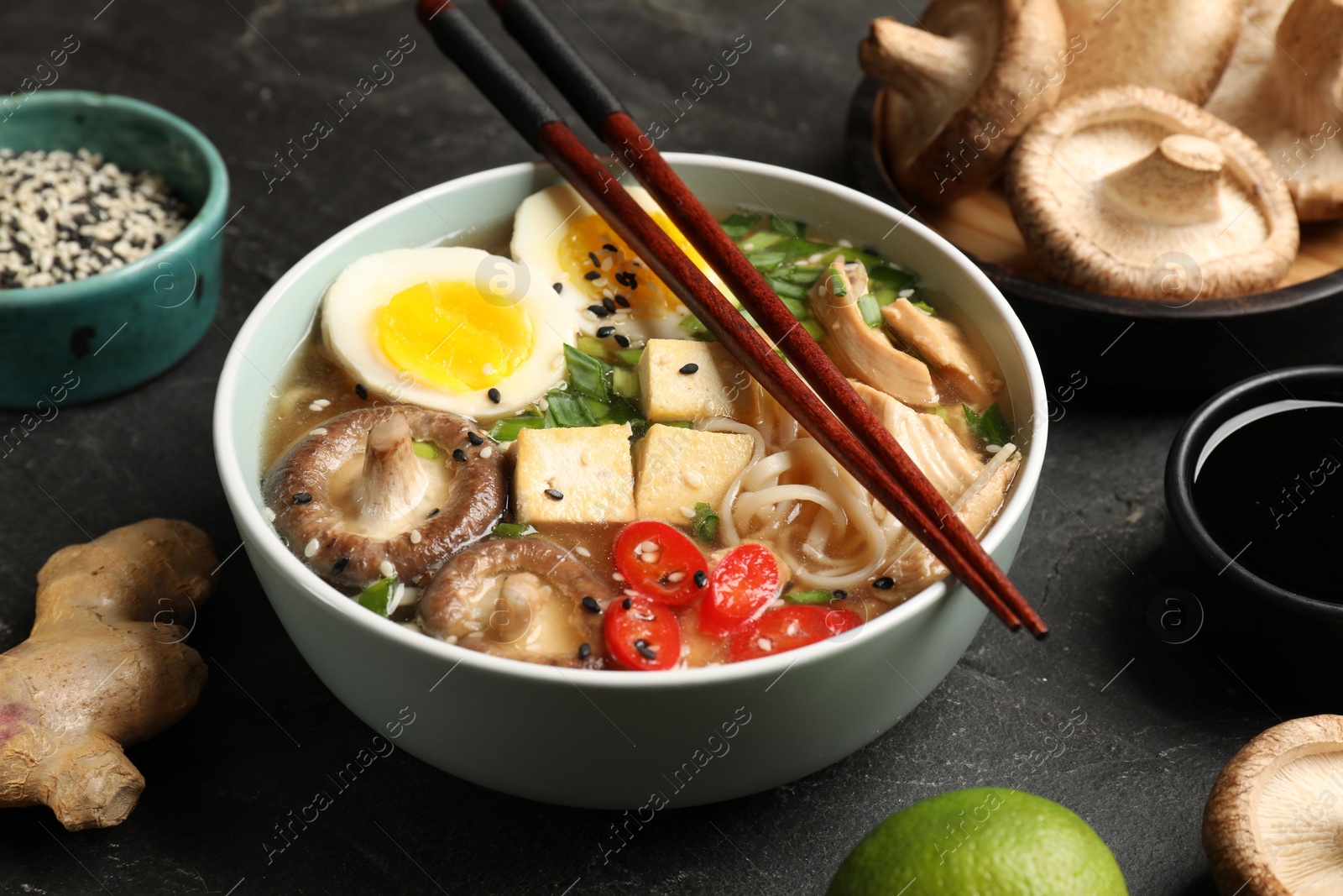 Photo of Noodle soup. Bowl of delicious ramen, ingredients and chopsticks on black table