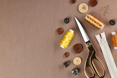 Photo of Different sewing supplies on brown fabric, flat lay. Space for text